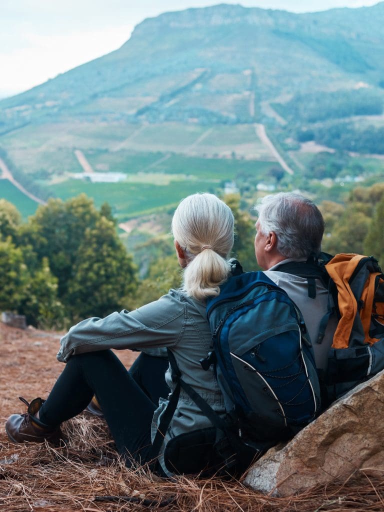 Senior couple sitting after hike looking over a valley as an example of redefining aging.