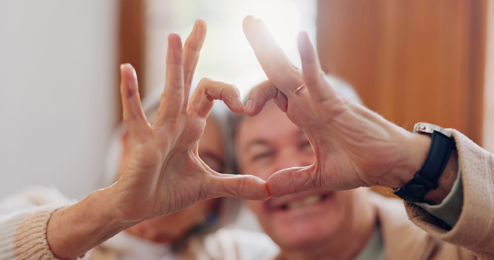 elderly couple creating a heart together with their hands
