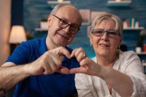 elderly man and woman holding hands in a shared heart shape.