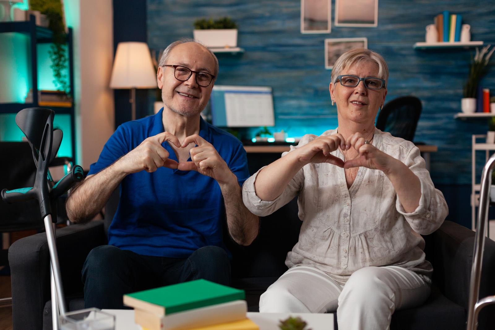 Elderly happy couple making heart sign with hands.